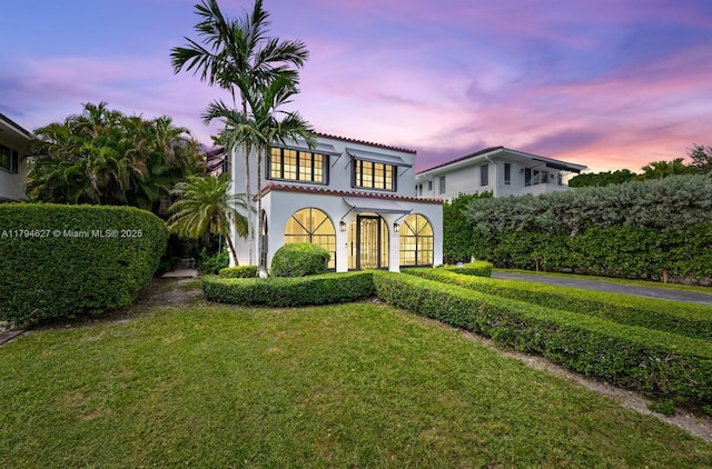 mediterranean / spanish-style home featuring stucco siding, driveway, a tile roof, and a front lawn