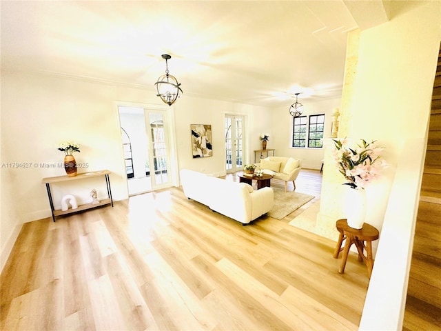 living room featuring baseboards, light wood-style flooring, crown molding, and a chandelier