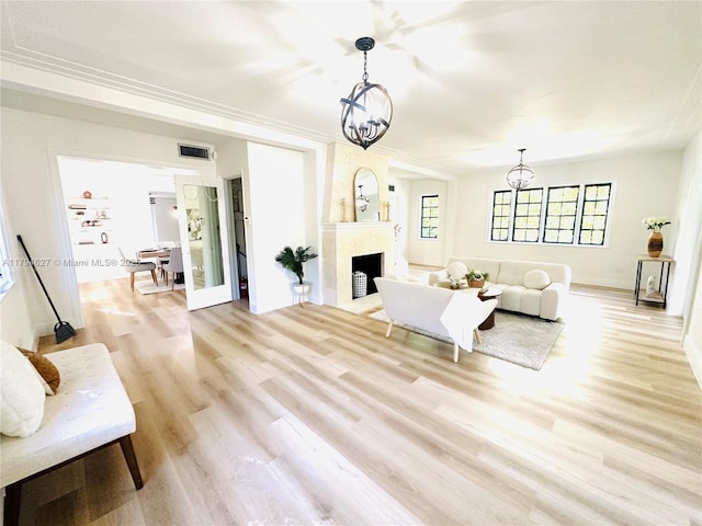 living room featuring light wood-style floors, visible vents, a fireplace, baseboards, and an inviting chandelier