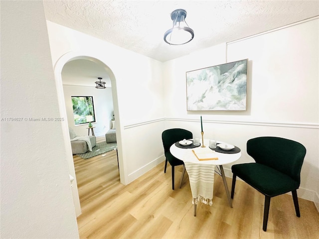 living area with a textured ceiling, baseboards, arched walkways, and wood finished floors