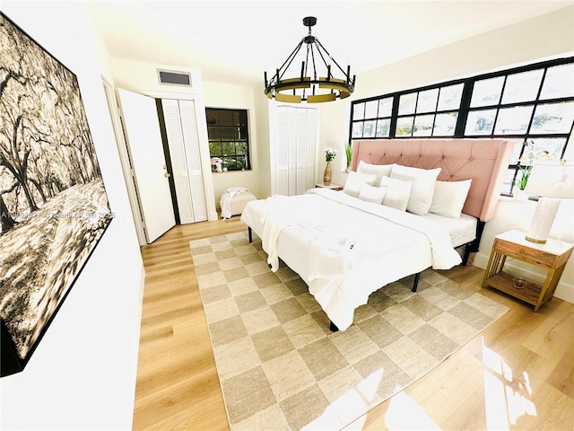 bedroom with multiple closets, light wood-type flooring, a chandelier, and visible vents