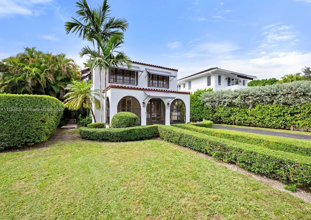 mediterranean / spanish-style home with stucco siding, a tile roof, a balcony, and a front lawn