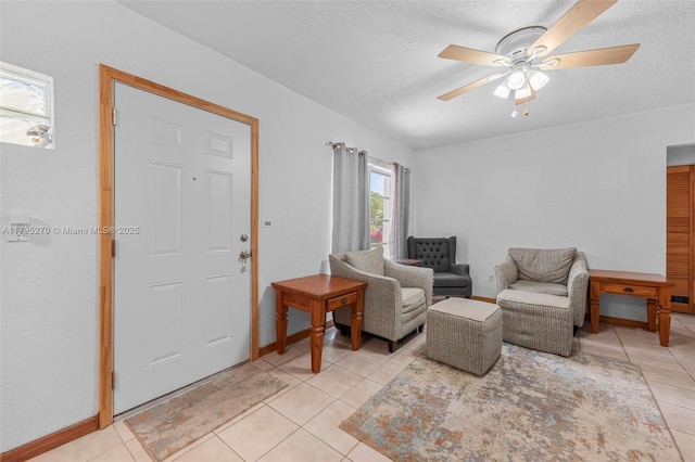 interior space featuring baseboards, a ceiling fan, a textured ceiling, and light tile patterned floors