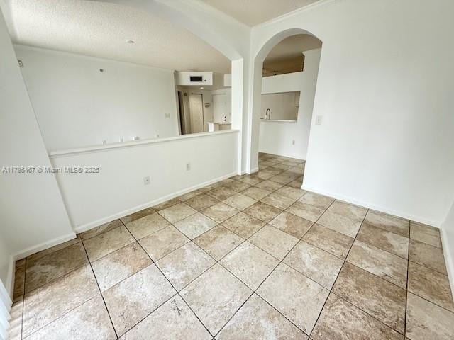 spare room featuring arched walkways, baseboards, light tile patterned floors, and a textured ceiling
