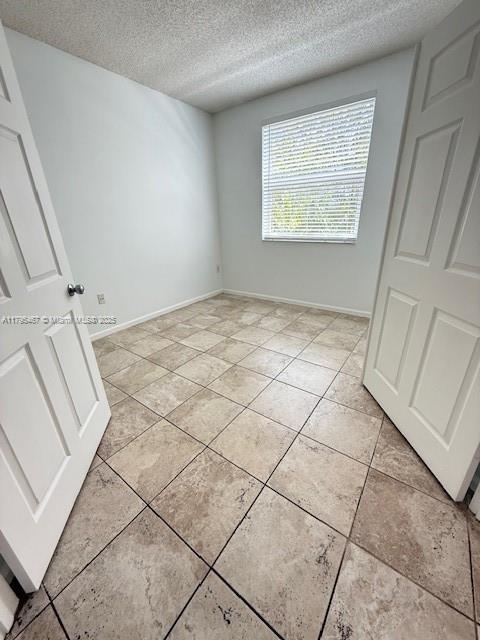 unfurnished bedroom featuring light tile patterned floors, baseboards, and a textured ceiling