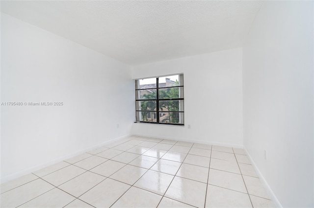empty room featuring light tile patterned floors, baseboards, and a textured ceiling