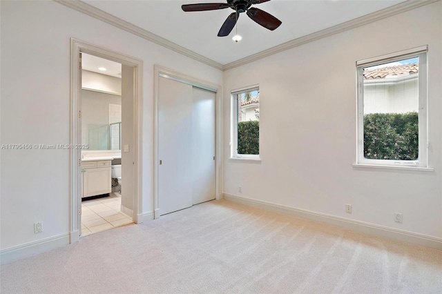 unfurnished bedroom with multiple windows, light carpet, ornamental molding, ensuite bathroom, and baseboards