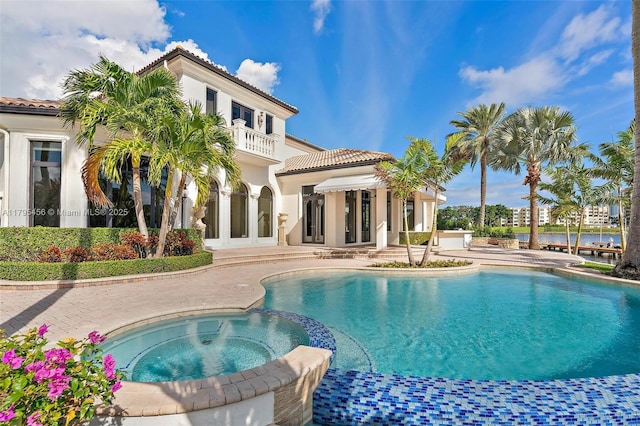 back of house with a balcony, a patio area, a tiled roof, a pool with connected hot tub, and stucco siding