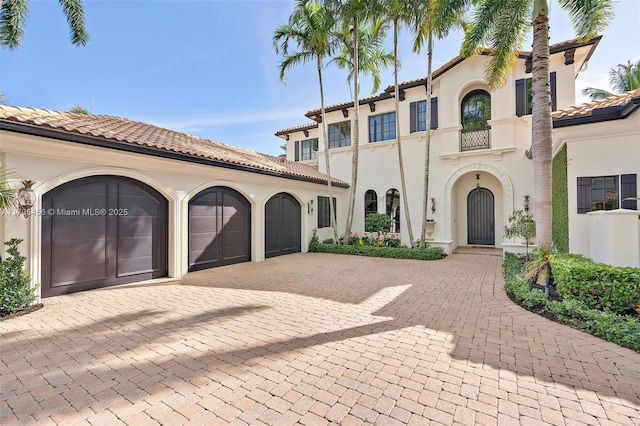 mediterranean / spanish house featuring decorative driveway, an attached garage, a tile roof, and stucco siding