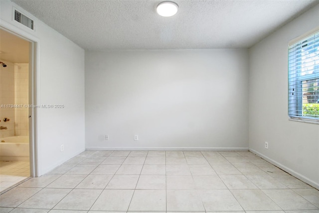 empty room featuring baseboards, a textured ceiling, visible vents, and light tile patterned floors