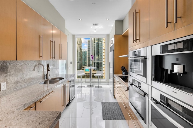 kitchen featuring a wall of windows, tasteful backsplash, light stone countertops, a sink, and beverage cooler