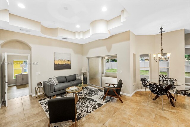 living room with baseboards, recessed lighting, a tray ceiling, a chandelier, and light tile patterned floors