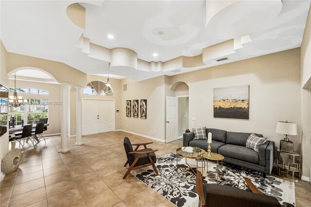 living room featuring an inviting chandelier, arched walkways, decorative columns, light tile patterned floors, and a towering ceiling