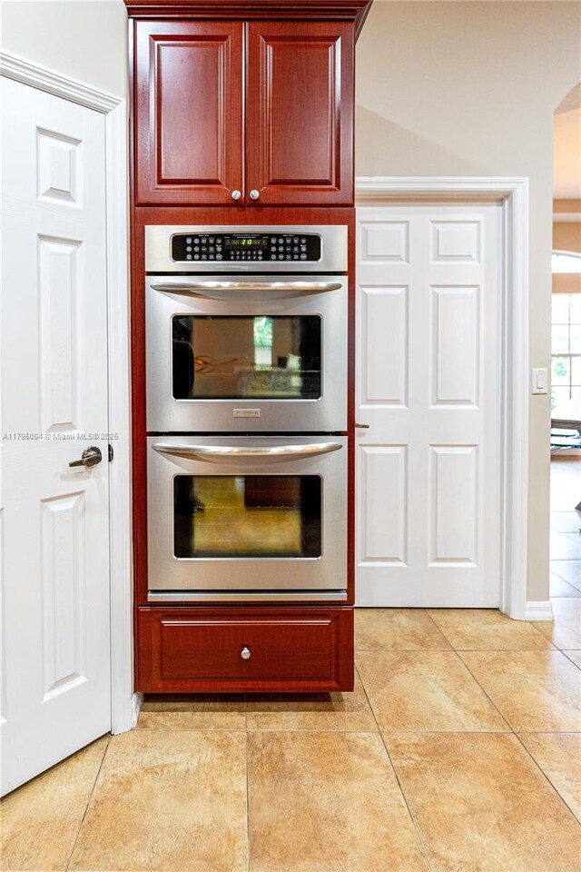 kitchen with reddish brown cabinets, stainless steel double oven, and light tile patterned floors