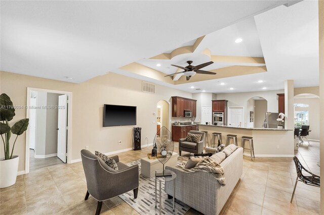 living room featuring ceiling fan, arched walkways, light tile patterned floors, a tray ceiling, and visible vents