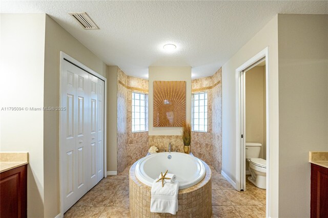 full bathroom featuring vanity, a garden tub, visible vents, toilet, and a textured ceiling