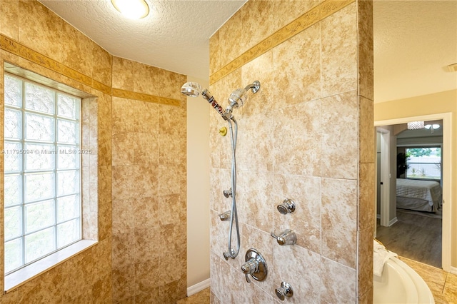 ensuite bathroom featuring a textured ceiling, a tile shower, and a wealth of natural light