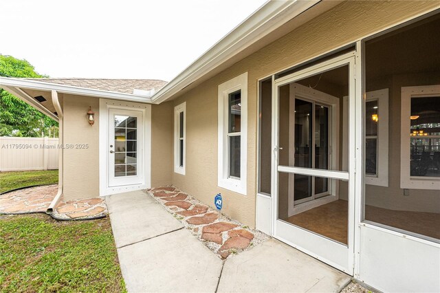 entrance to property with fence, stucco siding, and roof with shingles