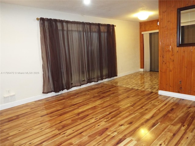 spare room with wooden walls, baseboards, and wood finished floors