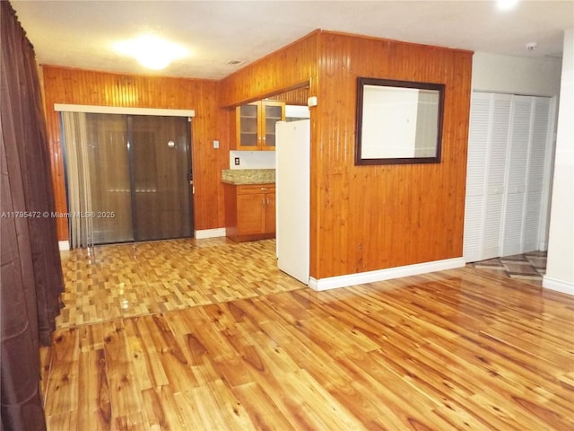 empty room featuring light wood-type flooring, wood walls, baseboards, and visible vents