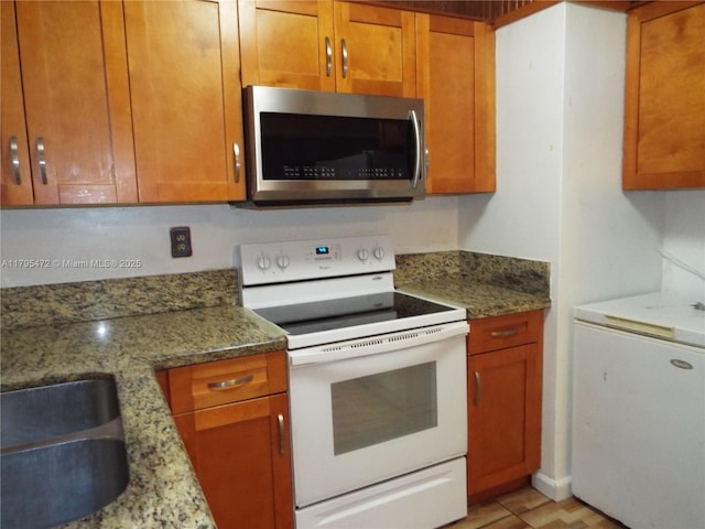 kitchen featuring a sink, brown cabinetry, white appliances, and light stone countertops