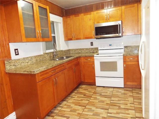 kitchen with white appliances, glass insert cabinets, light stone countertops, brown cabinets, and a sink