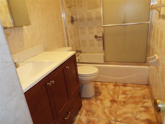 bathroom with tile walls, tile patterned flooring, bath / shower combo with glass door, vanity, and toilet