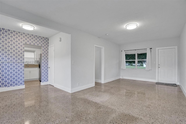 unfurnished room with baseboards, wallpapered walls, and speckled floor