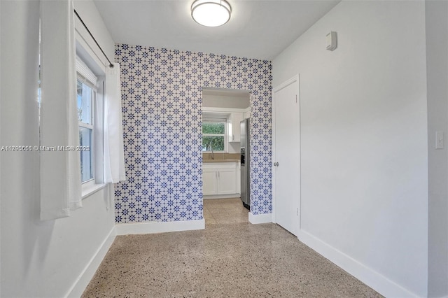 spare room featuring baseboards, light speckled floor, and wallpapered walls