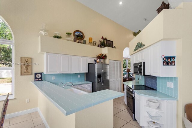 11613 NW 11th Pl, Coral Springs, FL 33071 - kitchen with white cabinets, light tile patterned flooring, appliances with stainless steel finishes, a peninsula, and a towering ceiling