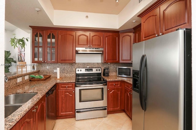kitchen featuring under cabinet range hood, light stone counters, backsplash, light tile patterned floors, and stainless steel appliances