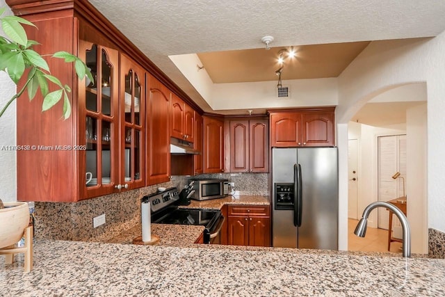 kitchen featuring under cabinet range hood, appliances with stainless steel finishes, decorative backsplash, and glass insert cabinets