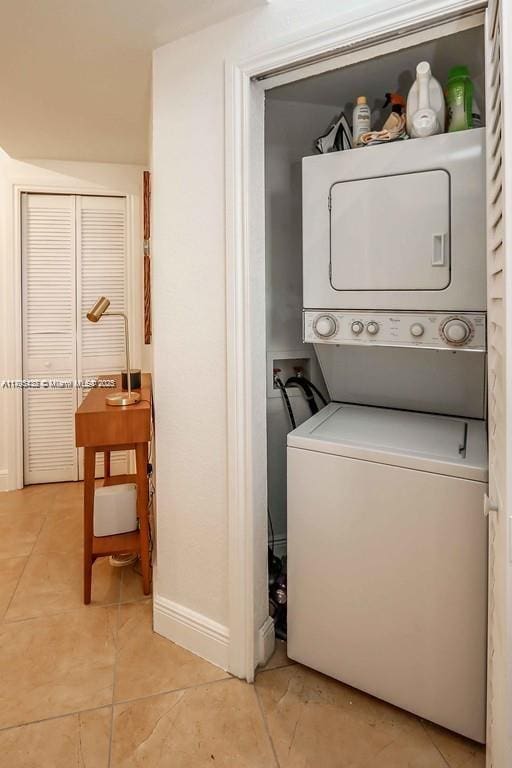 clothes washing area featuring laundry area, stacked washer and dryer, baseboards, and light tile patterned floors