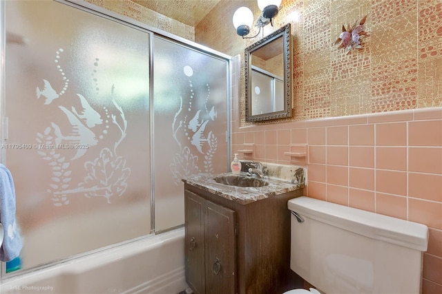 bathroom with vanity, tile walls, combined bath / shower with glass door, and toilet