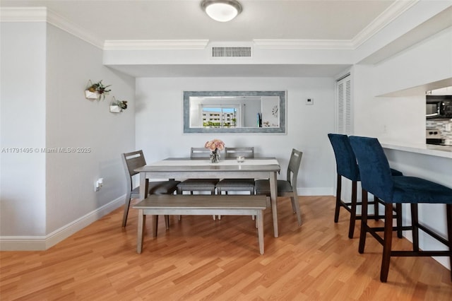 dining room featuring baseboards, ornamental molding, light wood finished floors, and visible vents