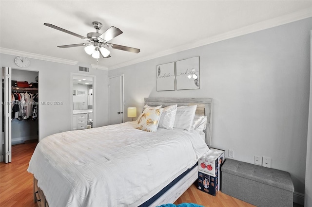 bedroom with a walk in closet, ornamental molding, wood finished floors, and visible vents
