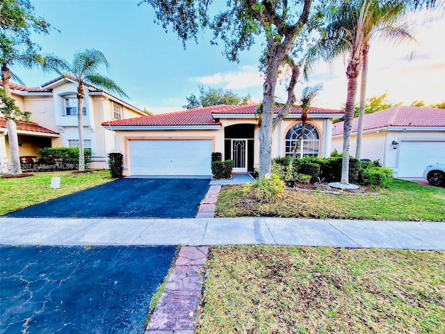 mediterranean / spanish house with an attached garage, aphalt driveway, stucco siding, and a tiled roof