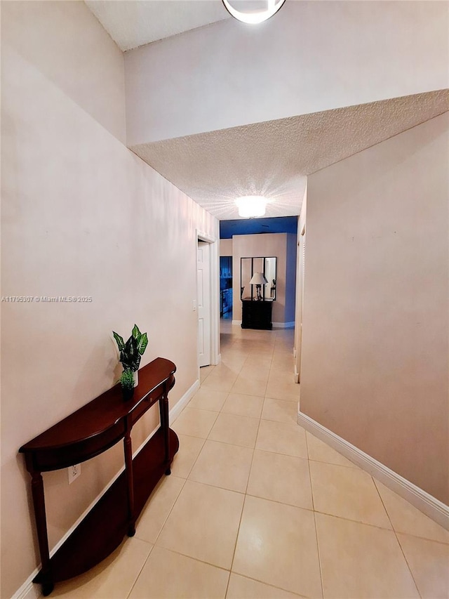 hallway with a textured ceiling, baseboards, and tile patterned flooring