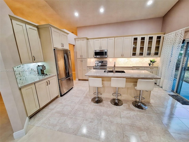 kitchen featuring a kitchen breakfast bar, appliances with stainless steel finishes, tasteful backsplash, light stone countertops, and a sink