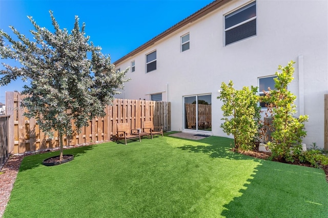rear view of house featuring a lawn, fence private yard, and stucco siding