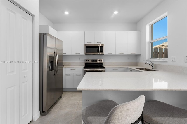 kitchen with appliances with stainless steel finishes, light stone countertops, a sink, a peninsula, and recessed lighting