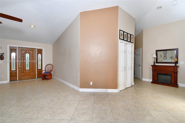 foyer featuring light tile patterned floors, a ceiling fan, baseboards, a glass covered fireplace, and vaulted ceiling