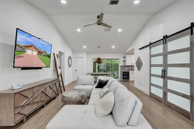 living room with a barn door, light wood finished floors, ceiling fan, and vaulted ceiling