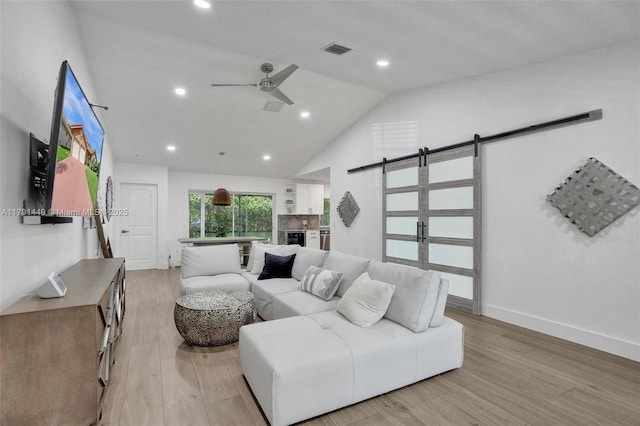 living room featuring ceiling fan, a barn door, high vaulted ceiling, light wood-style flooring, and visible vents