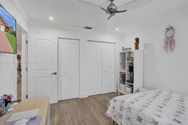 bedroom with ornamental molding, two closets, wood finished floors, and visible vents