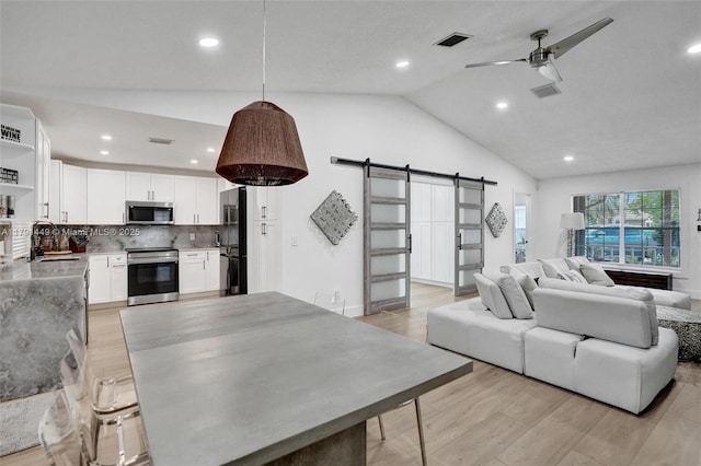 living room with ceiling fan, a barn door, light wood-style flooring, vaulted ceiling, and visible vents