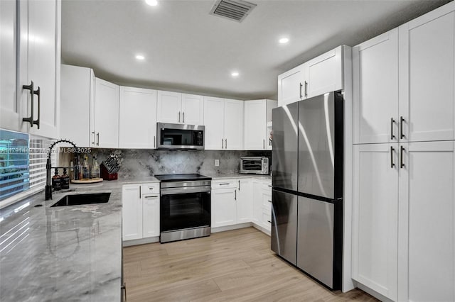 kitchen with white cabinets, light stone countertops, appliances with stainless steel finishes, a sink, and visible vents