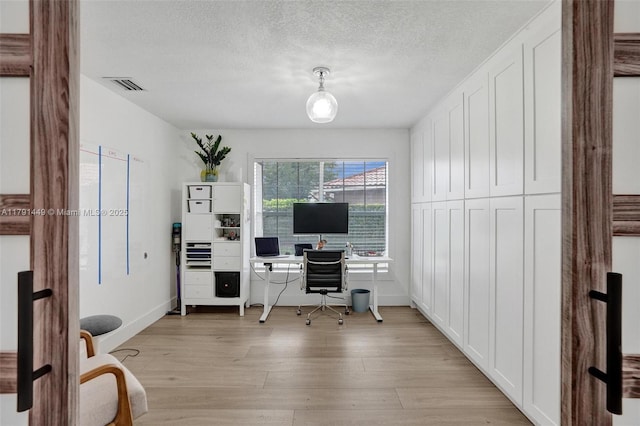 office space featuring baseboards, a textured ceiling, visible vents, and light wood-style flooring