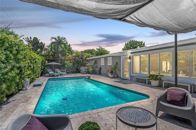 pool at dusk with a patio and an outdoor pool