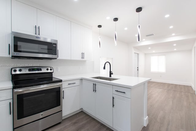 kitchen with a peninsula, light countertops, a sink, light wood finished floors, and stainless steel appliances